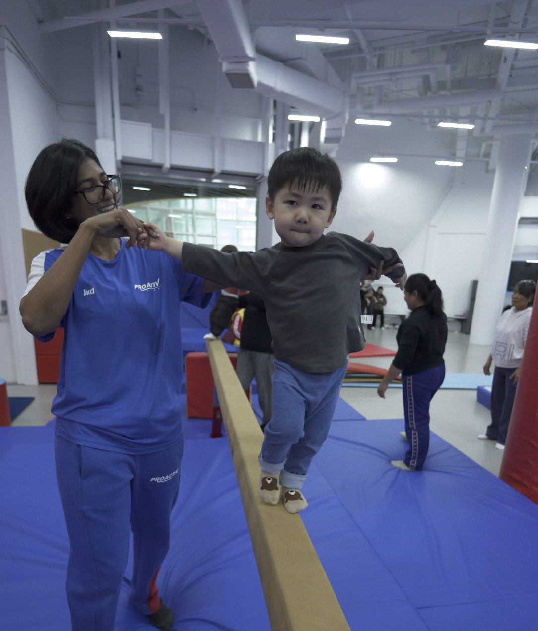Coach supporting toddler walking along a balance beam at ProGym