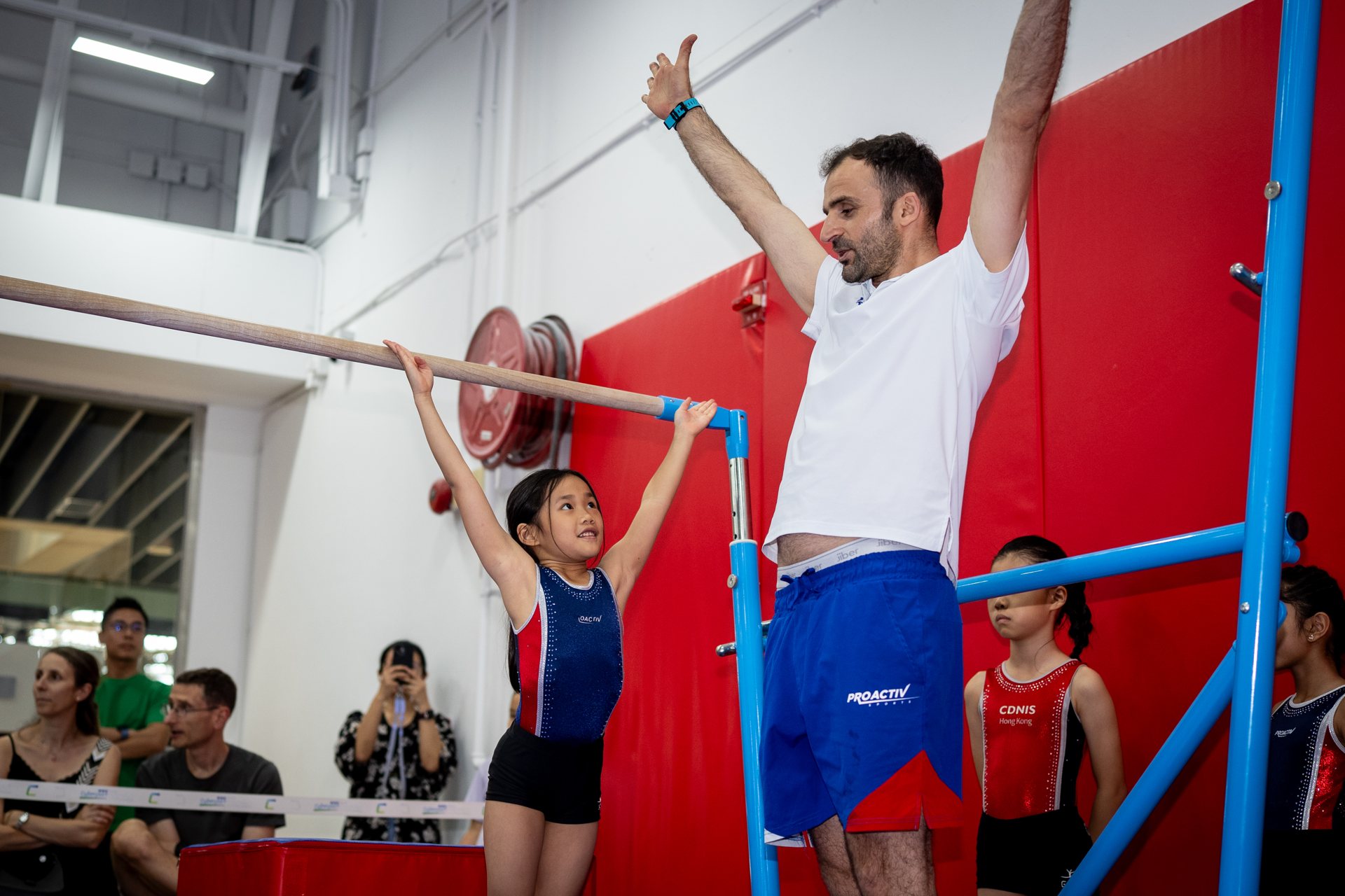 Coach supporting a gymnast on the bar during a ProActiv Sports competition