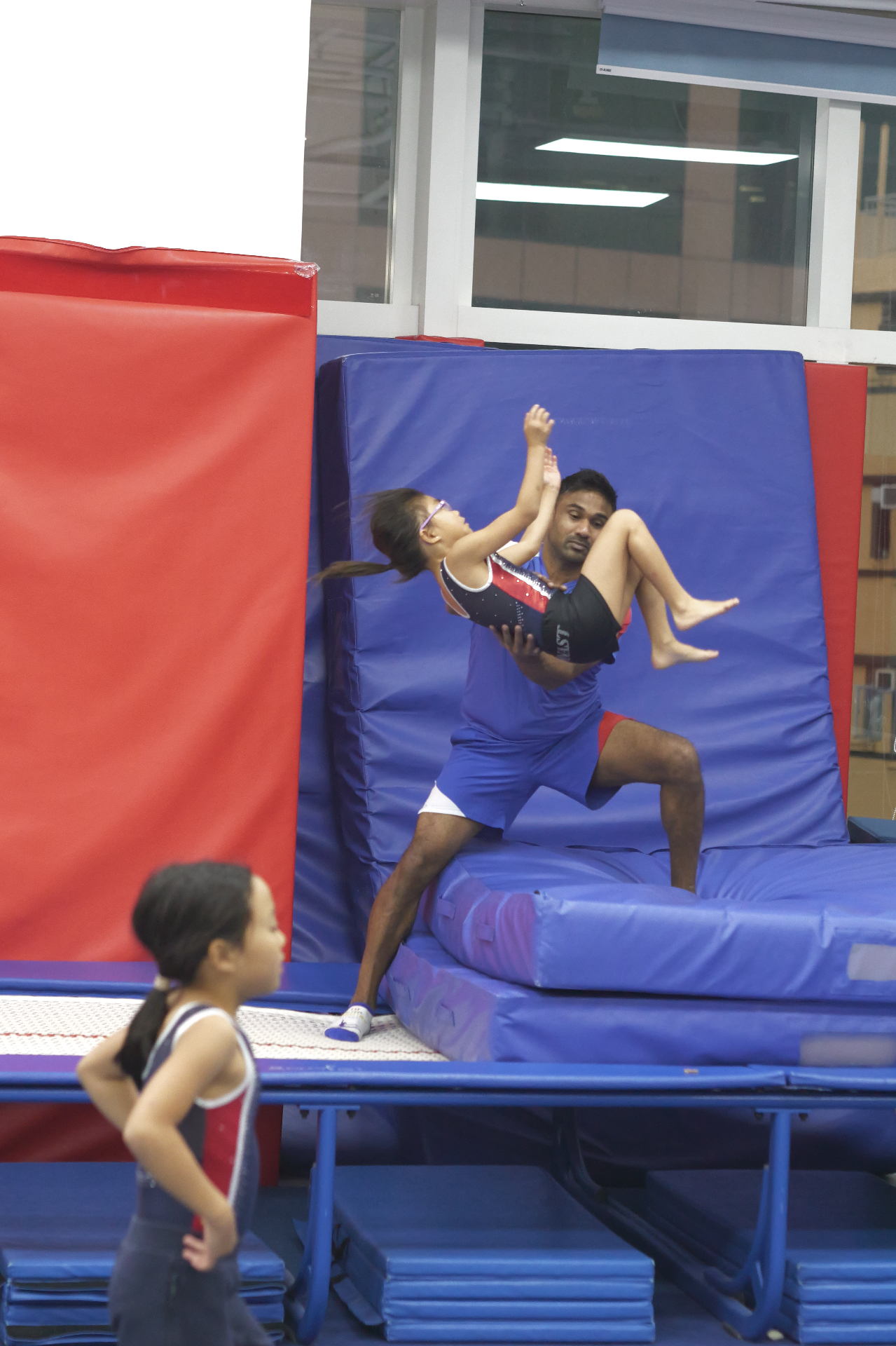 Coach spotting gymnast on incline mat during recreational class