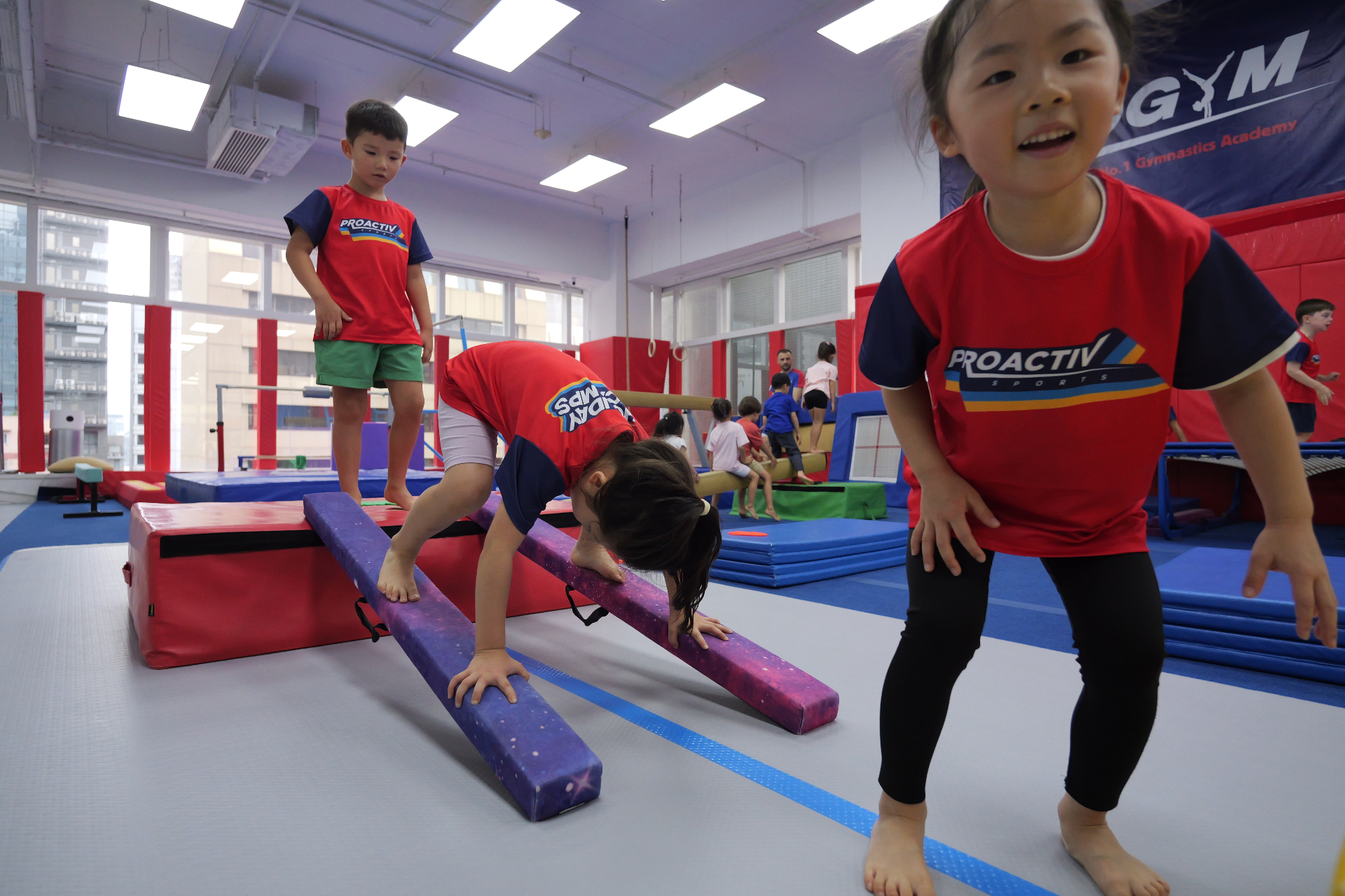 Children navigating a balance beam obstacle at a ProActiv Hong Kong Gymnastics Camp