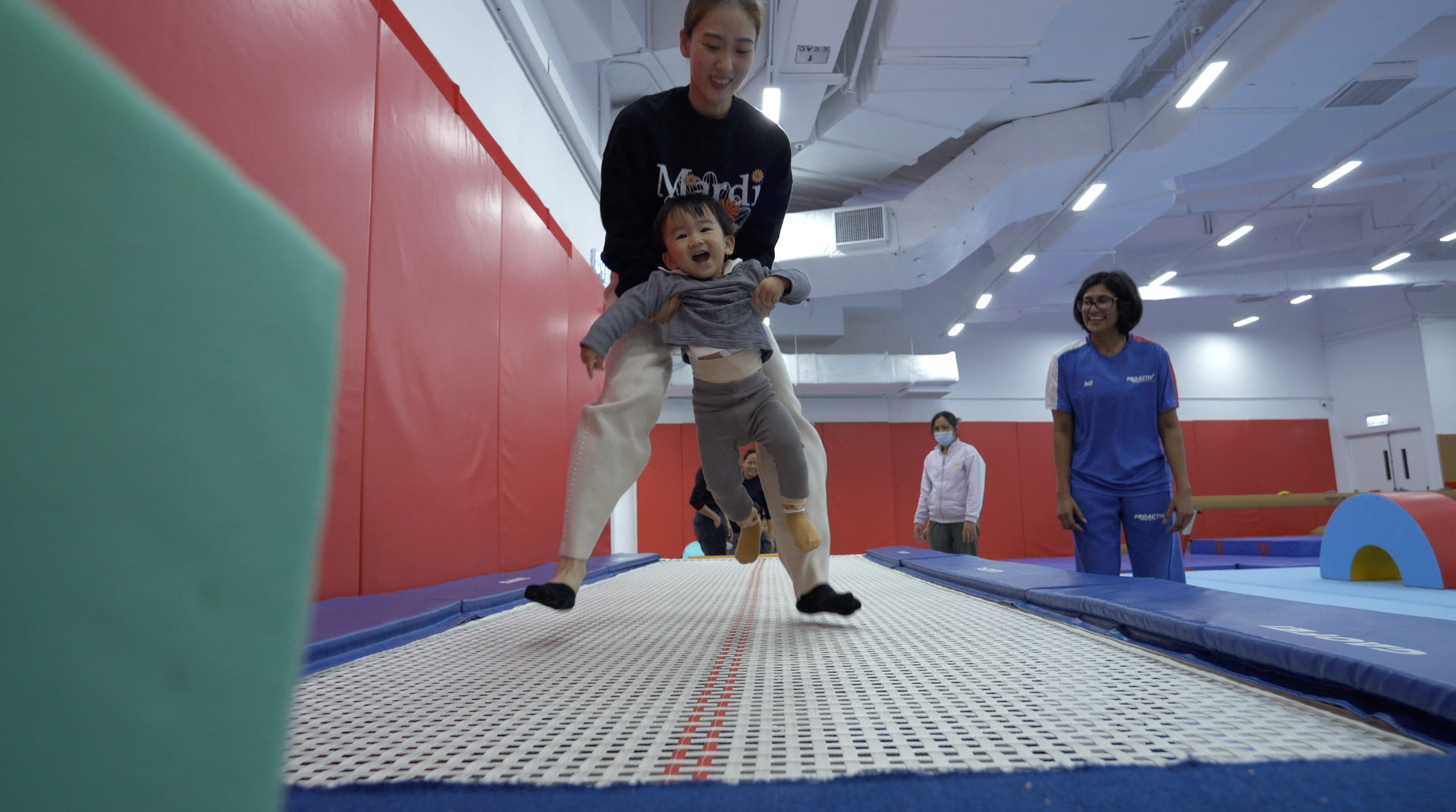 Toddler bouncing on trampoline with coach support at ProGym