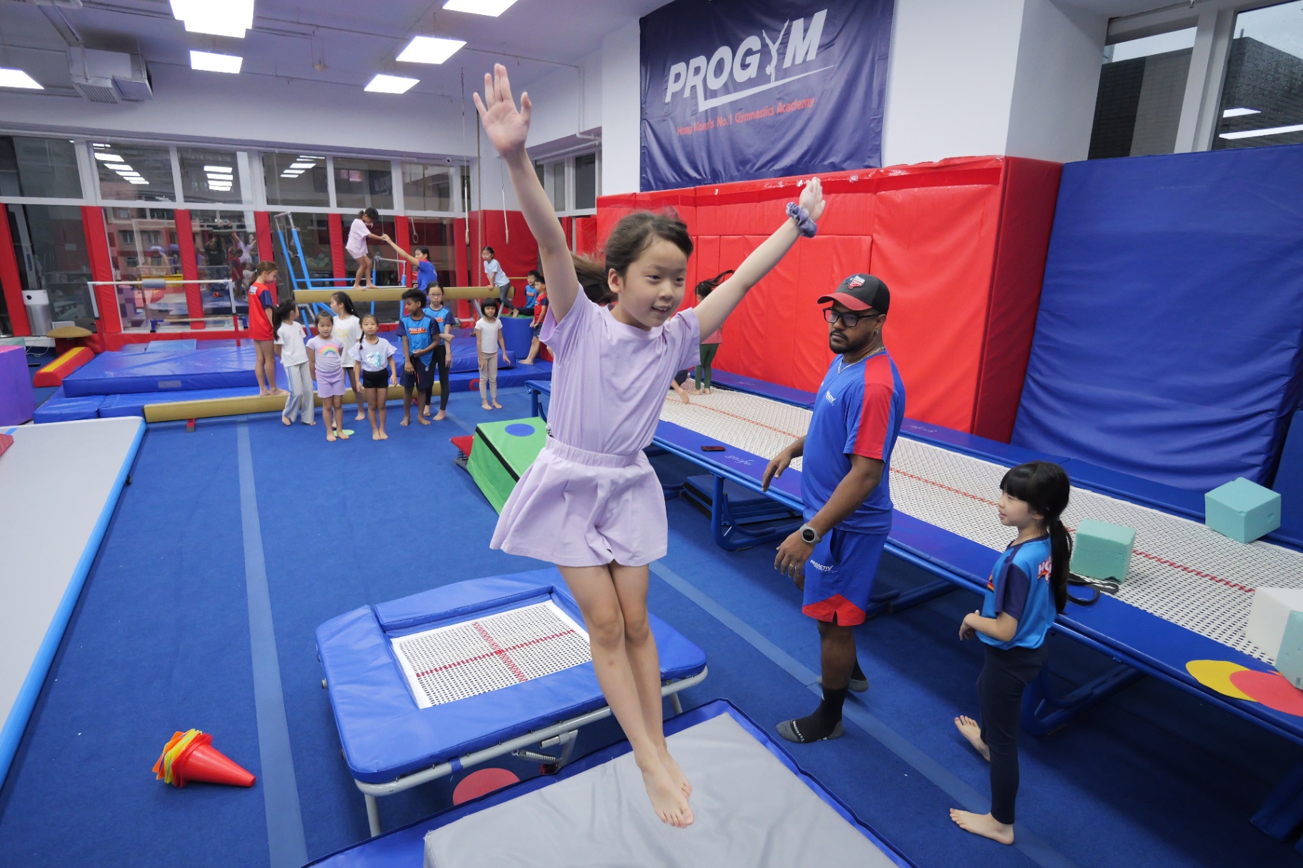 Gymnast landing a trampoline jump with a coach spotting at a ProActiv Hong Kong Gymnastics Camp