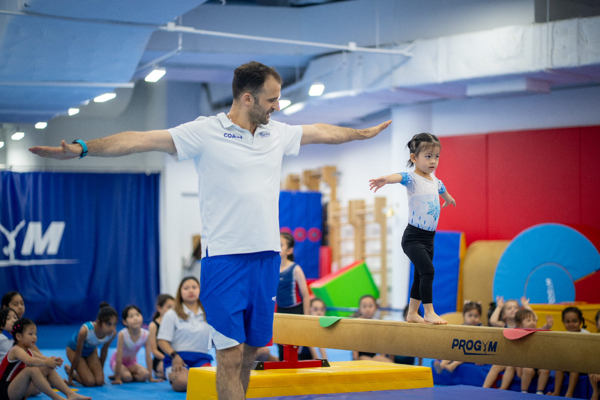 Coach guiding a young beginner gymnast on the beam at ProGym