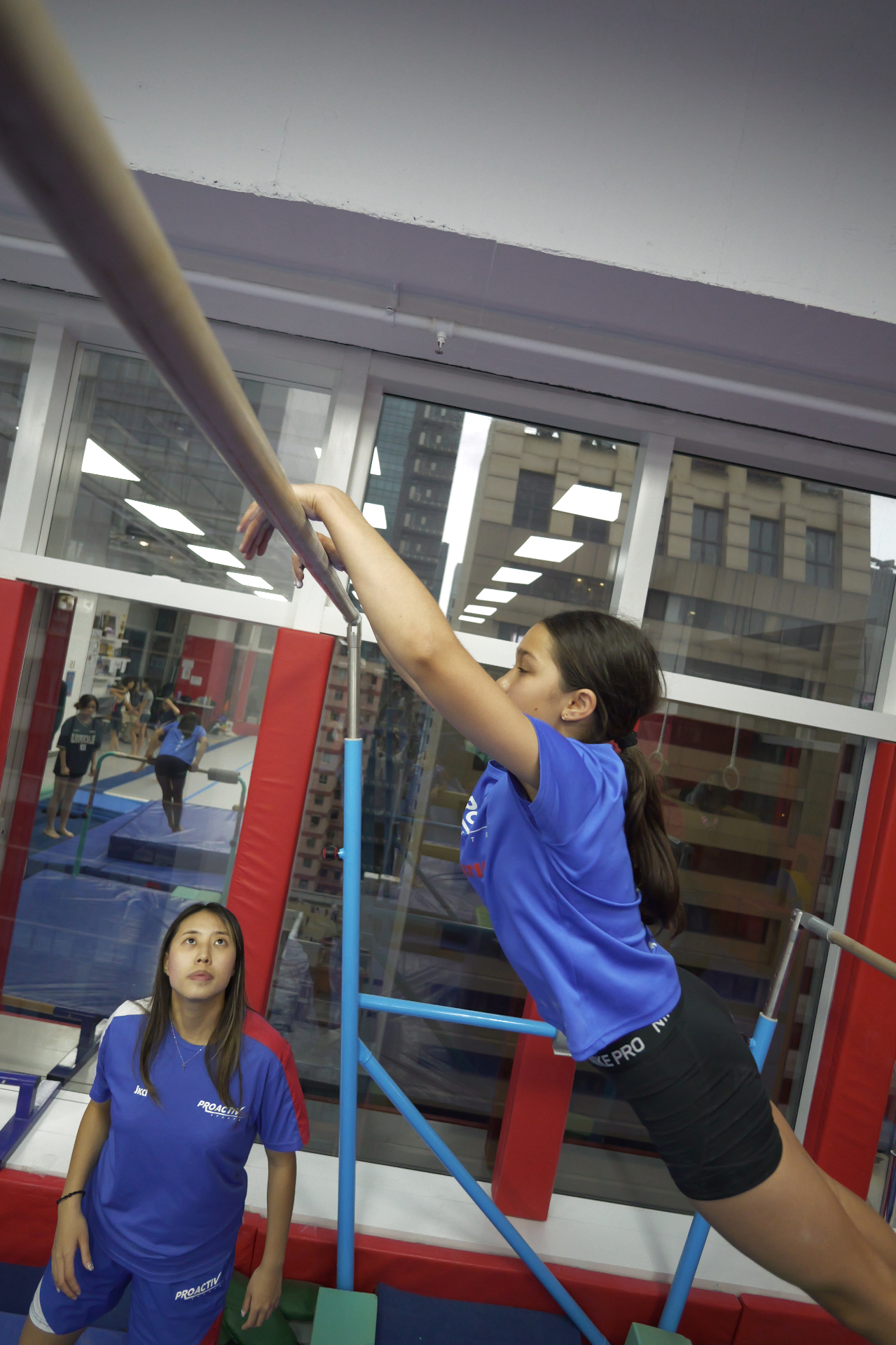 Competitive gymnast training on bars with coach supervision