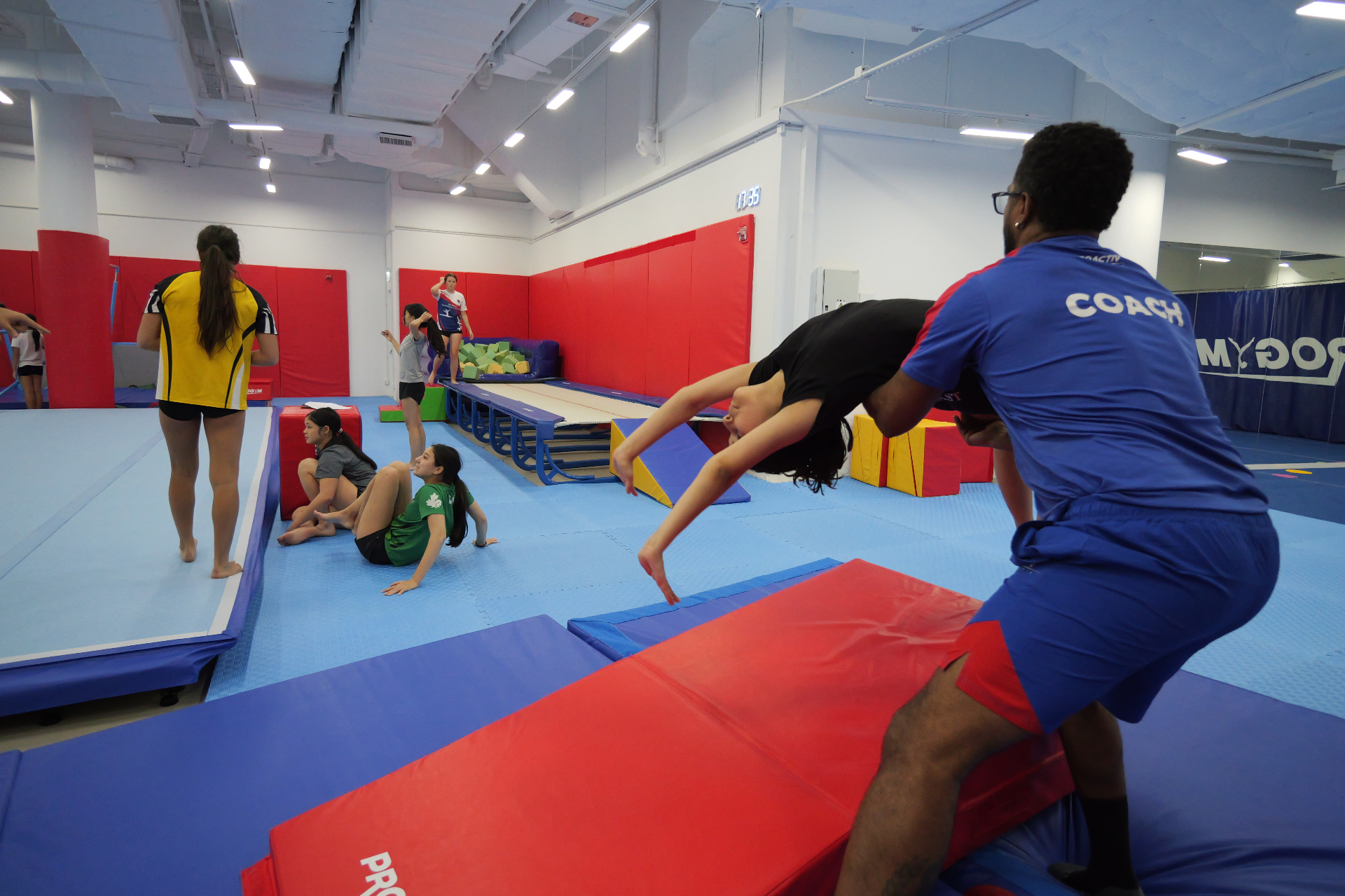 Coach spotting back tumbling on soft mats at ProGym