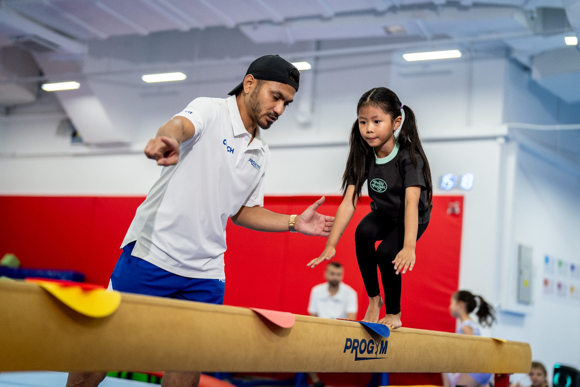 Coach guiding a young gymnast on the balance beam at a ProActiv Hong Kong Gymnastics Camp