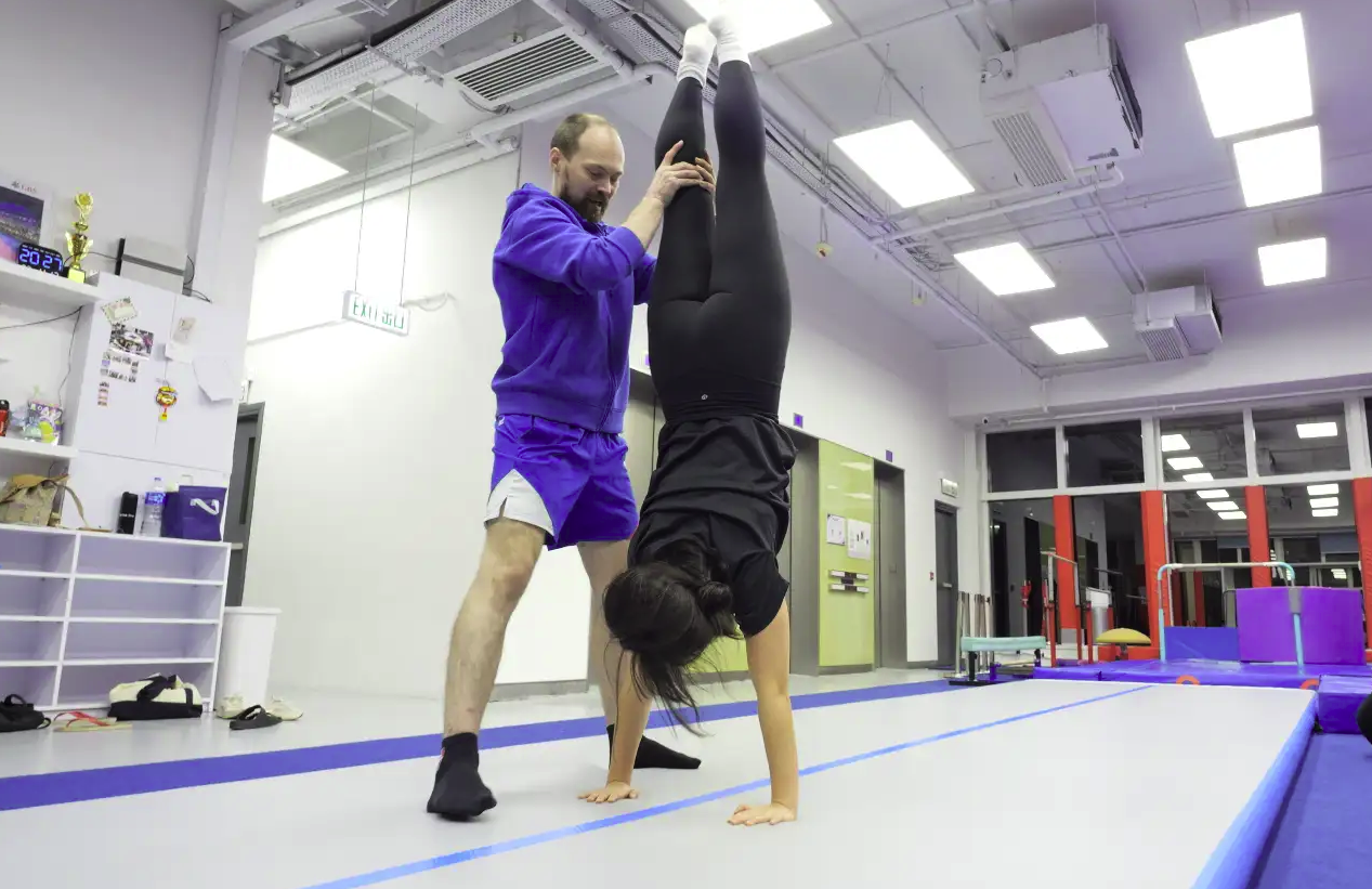 Adult gymnast practising handstand with coach spotting