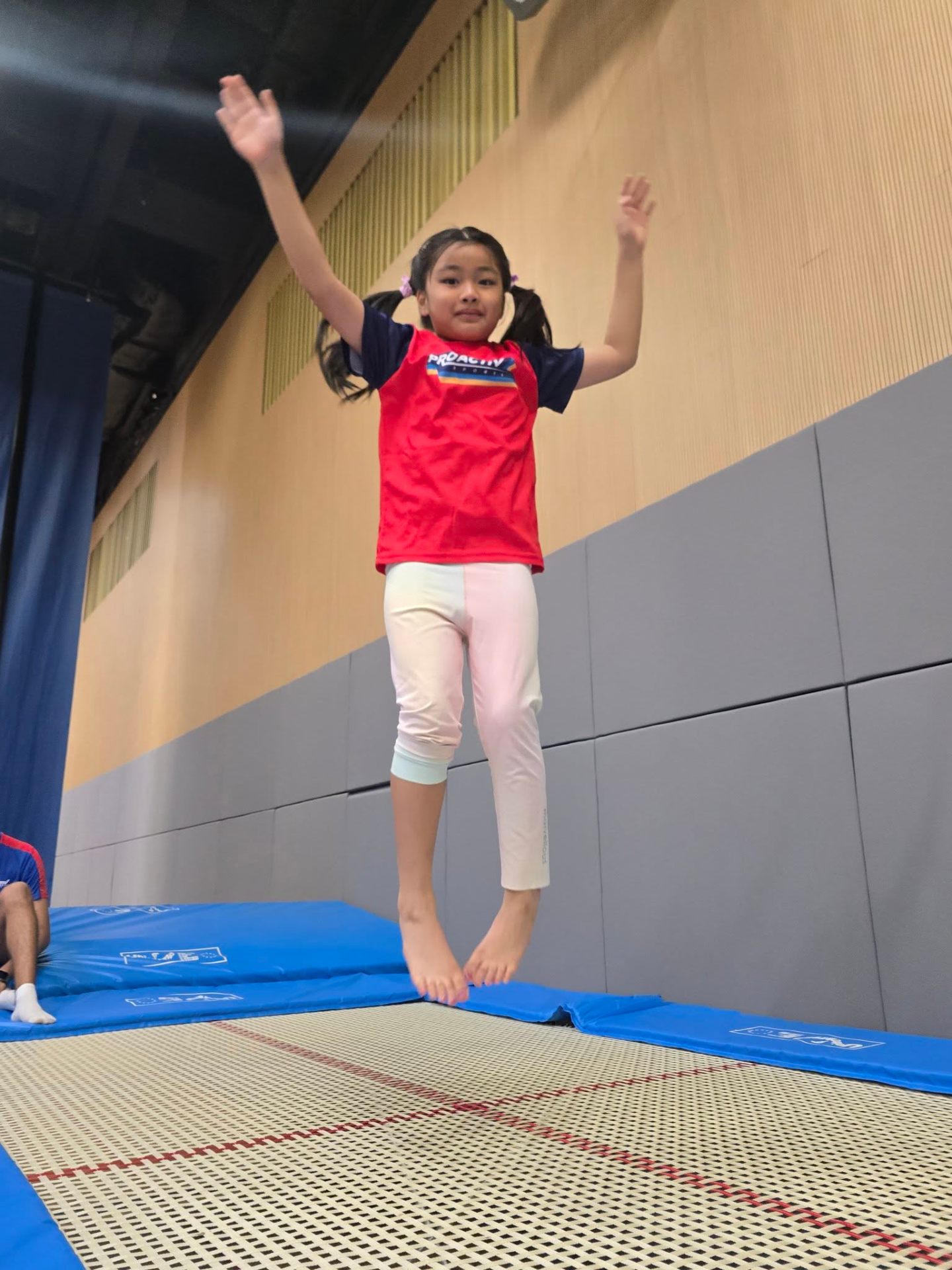 Child in a ProActiv shirt jumping on the trampoline at a Hong Kong Gymnastics Camp