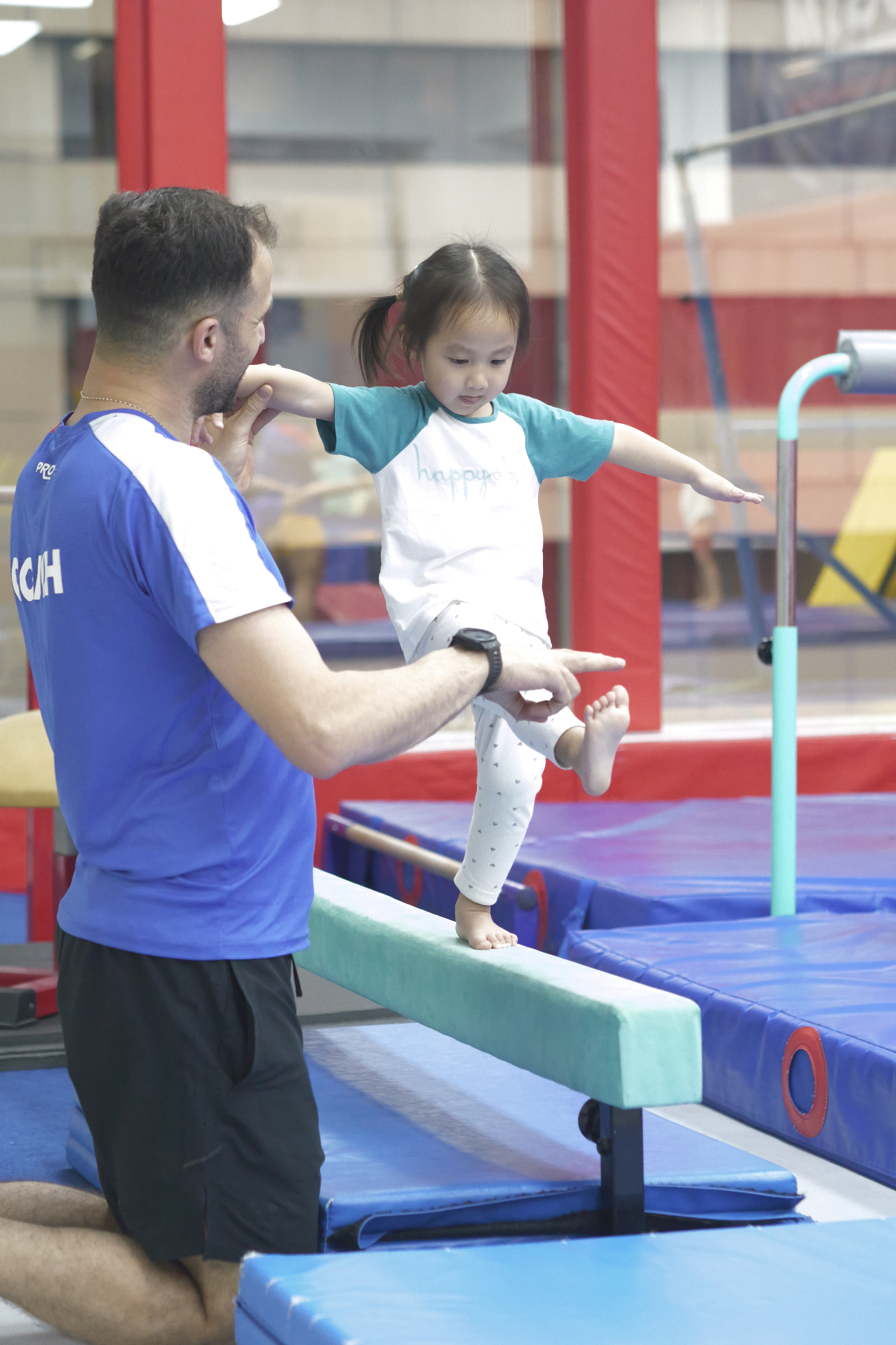 Coach coaching a toddler on the low beam during a private gymnastics class