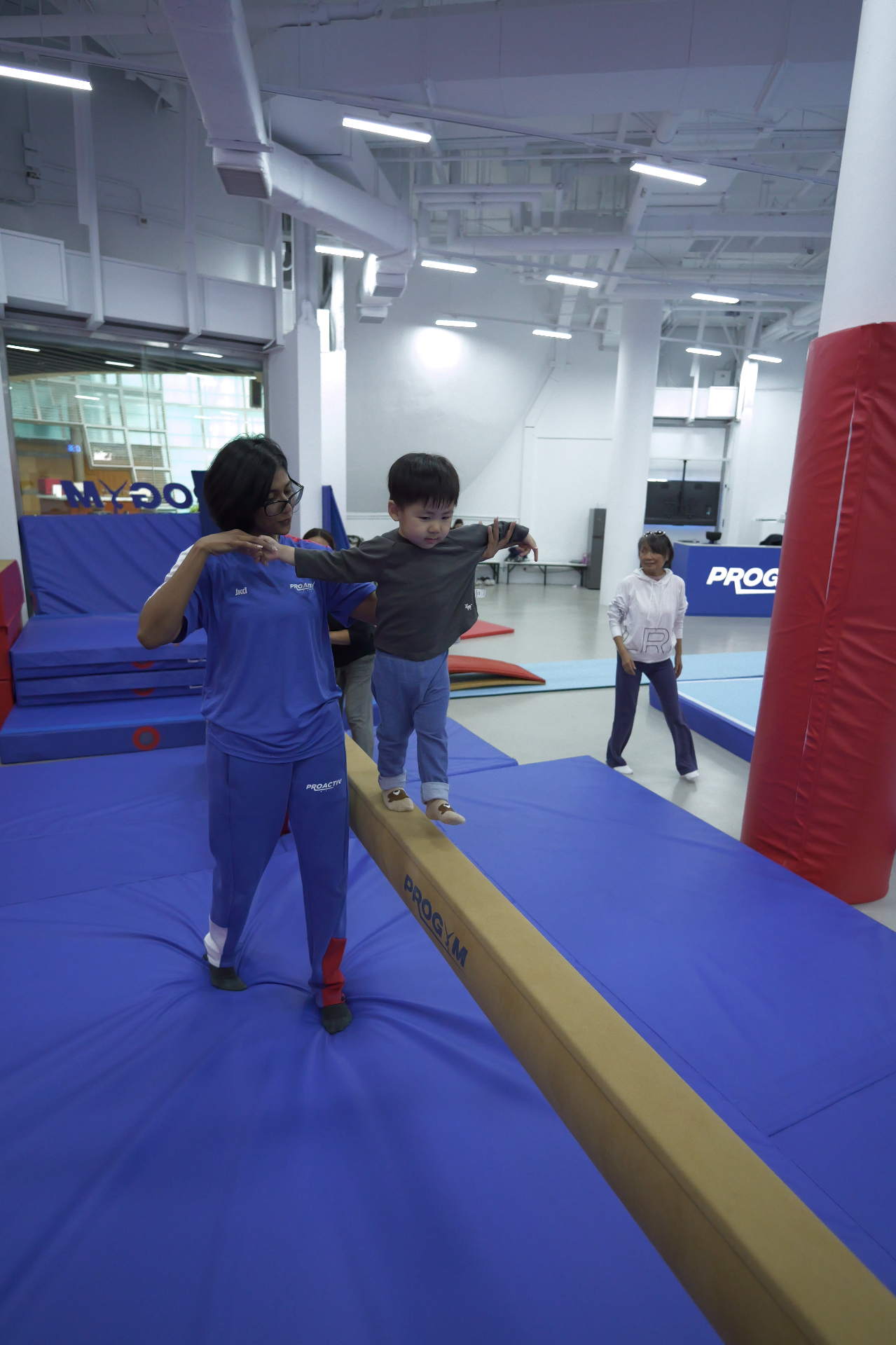 Coach guiding toddler across balance beam at ProGym