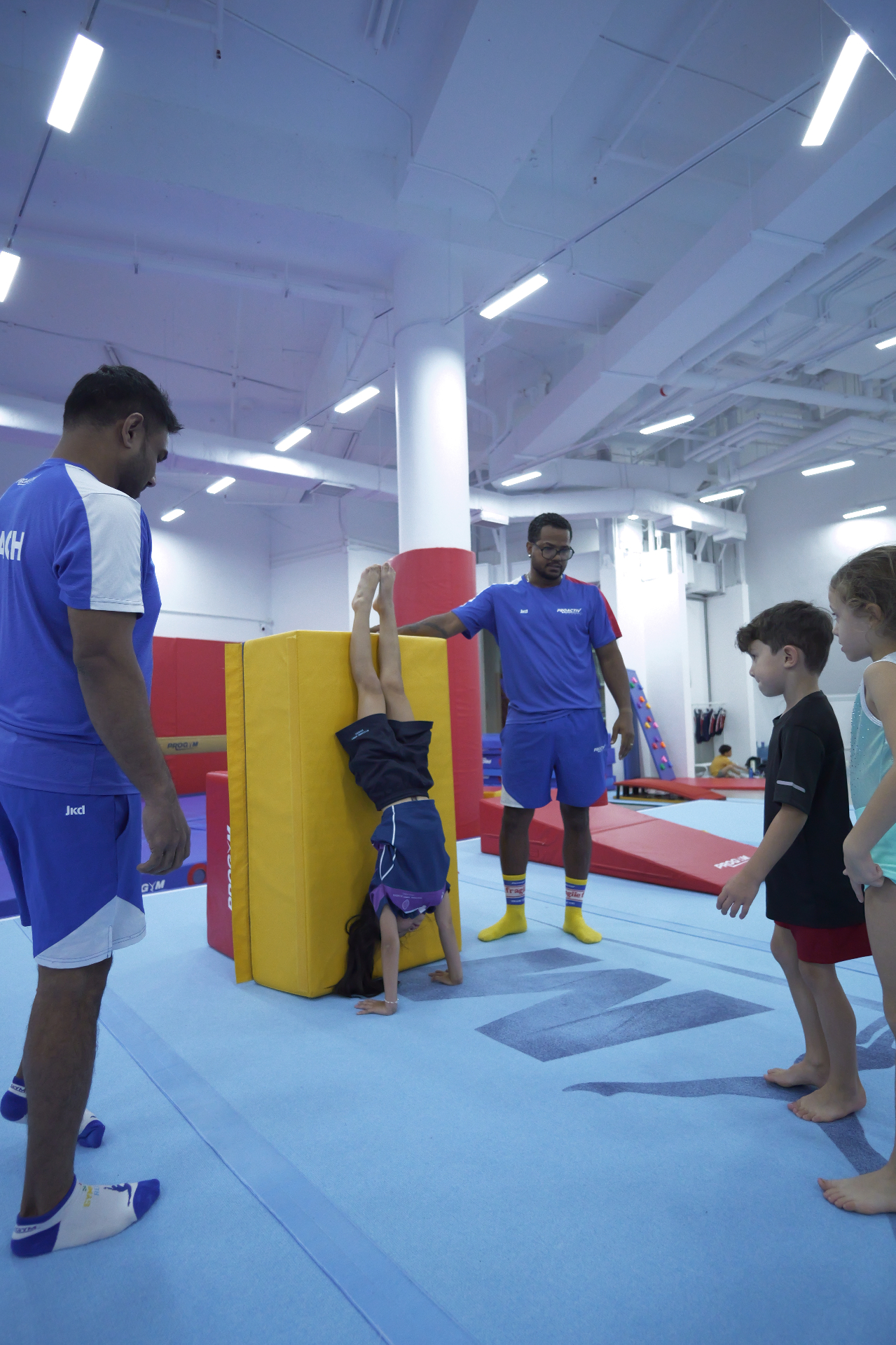 Child practising handstand against wall with coach support